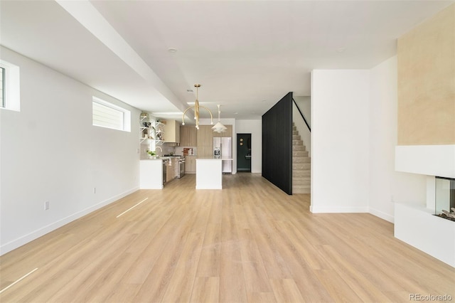 unfurnished living room featuring stairway, light wood-style flooring, and baseboards