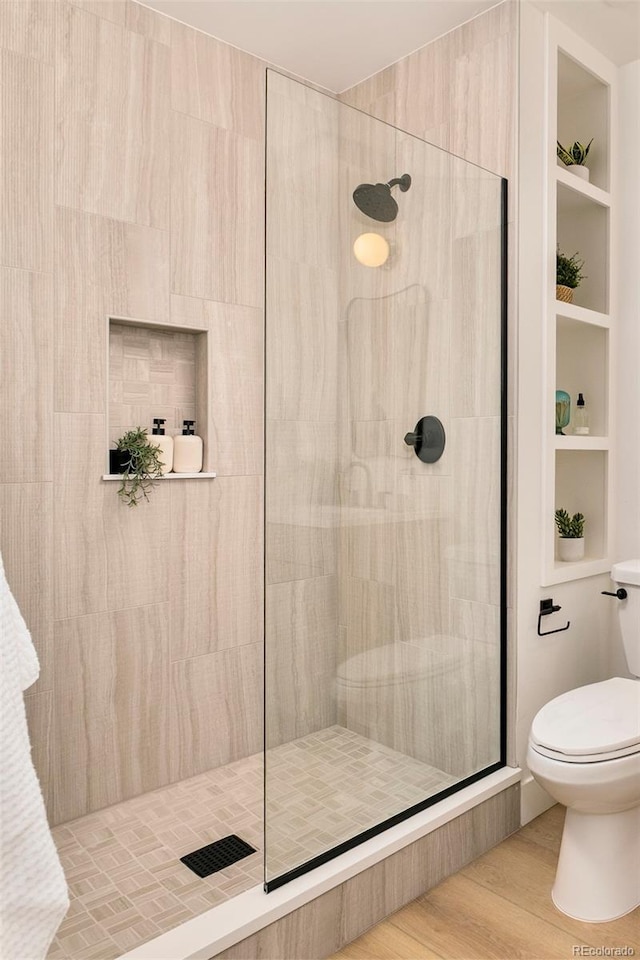 full bath featuring toilet, tiled shower, and wood finished floors