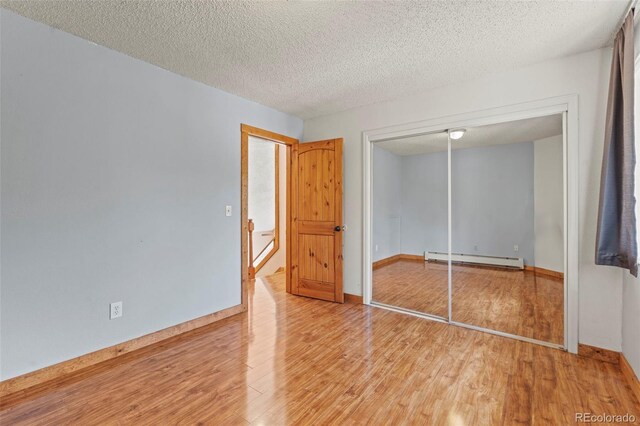 1345 Leslie Cir, Woodland Park, CO 80863 - unfurnished bedroom featuring a baseboard heating unit, light wood finished floors, a closet, and a textured ceiling