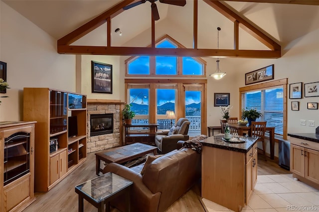 living room with high vaulted ceiling, light wood-type flooring, ceiling fan, beamed ceiling, and a stone fireplace