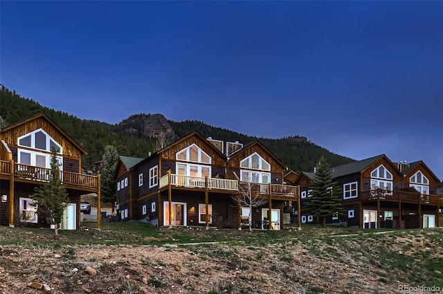 back of property featuring a deck with mountain view and a view of trees