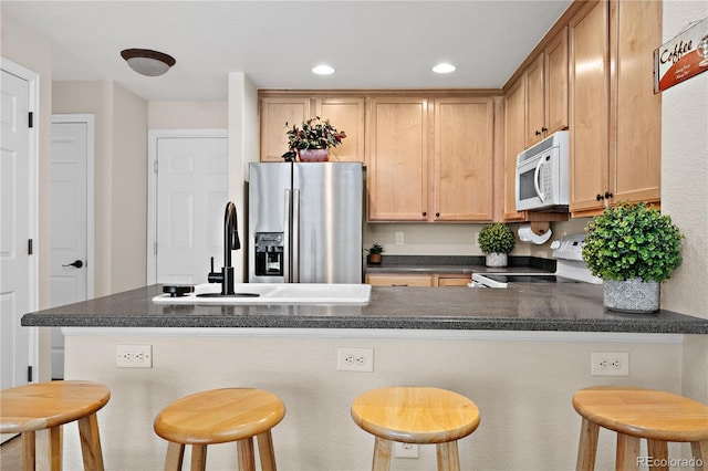 kitchen featuring sink, white appliances, a kitchen bar, light brown cabinetry, and kitchen peninsula