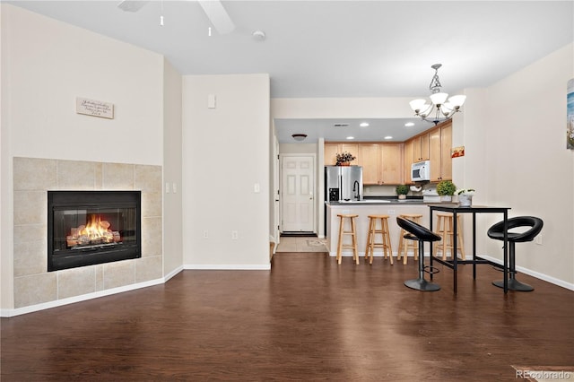 kitchen featuring white microwave, a kitchen breakfast bar, stainless steel refrigerator with ice dispenser, dark wood-type flooring, and dark countertops