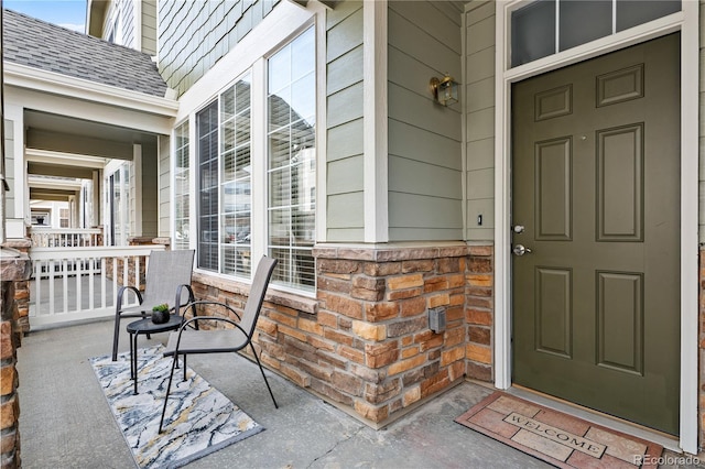 entrance to property featuring a porch and roof with shingles