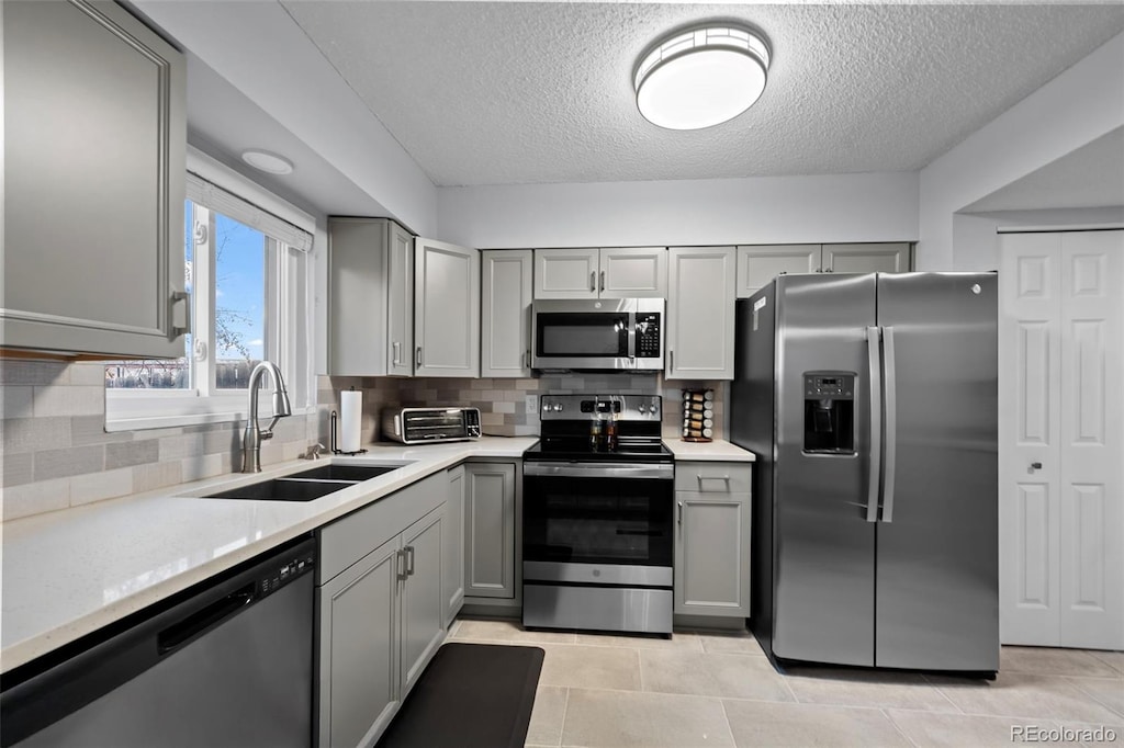 kitchen with gray cabinetry, sink, backsplash, appliances with stainless steel finishes, and light tile patterned flooring