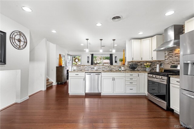 7132 Xavier Way, Westminster, CO 80030 - kitchen with stainless steel appliances, wall chimney range hood, a peninsula, decorative backsplash, and white cabinets