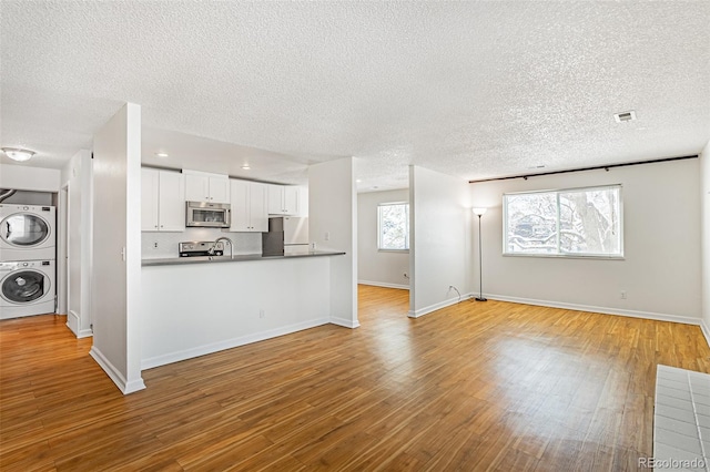 kitchen with stainless steel microwave, stacked washer / dryer, open floor plan, wood finished floors, and fridge