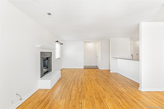 unfurnished living room featuring baseboards, visible vents, a tiled fireplace, light wood-style flooring, and a textured ceiling