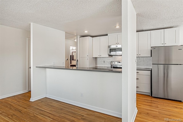 kitchen featuring tasteful backsplash, appliances with stainless steel finishes, white cabinets, wood finished floors, and baseboards