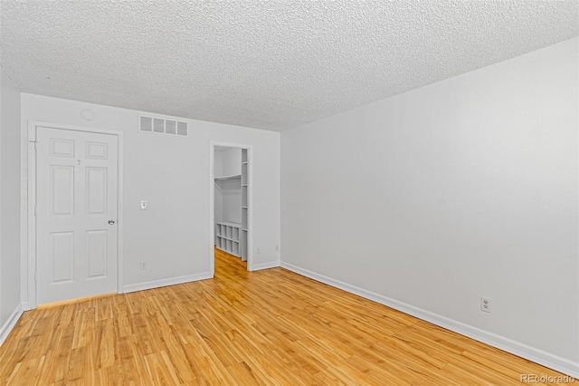 unfurnished room with light wood-type flooring, visible vents, a textured ceiling, and baseboards