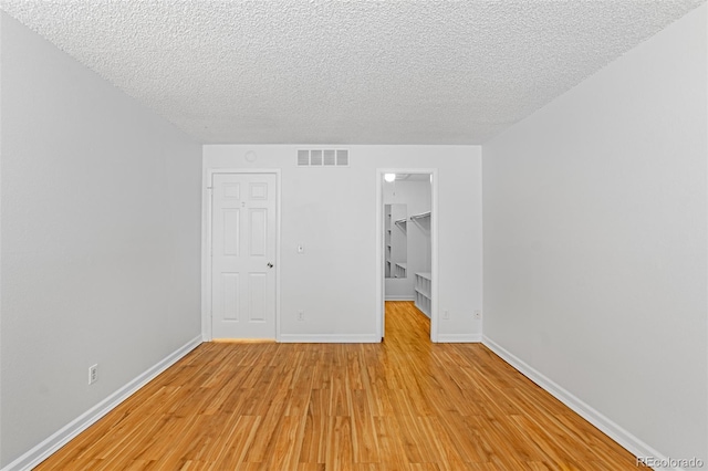 unfurnished bedroom with a closet, visible vents, light wood-style flooring, a spacious closet, and a textured ceiling