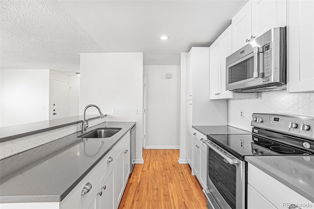 kitchen featuring a sink, stainless steel appliances, white cabinetry, backsplash, and light wood-style floors