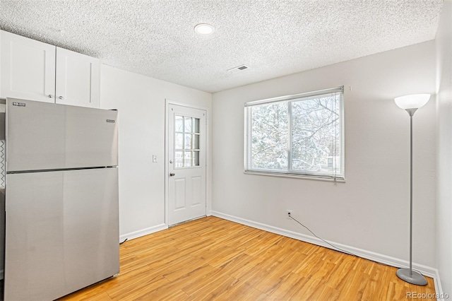 kitchen featuring freestanding refrigerator, white cabinets, light wood-type flooring, a textured ceiling, and baseboards