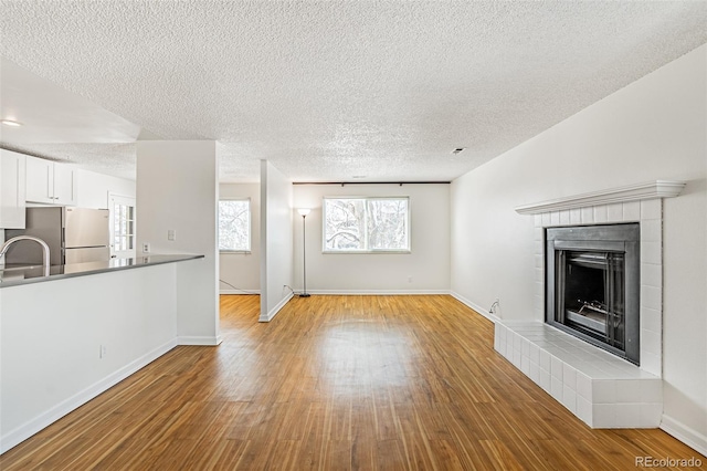 unfurnished living room featuring baseboards, a tile fireplace, a textured ceiling, and wood finished floors