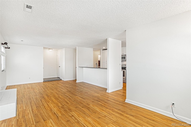 unfurnished living room with a textured ceiling, baseboards, visible vents, and light wood-style floors