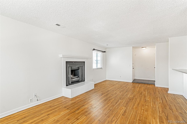 unfurnished living room with light wood finished floors, a textured ceiling, and a tiled fireplace