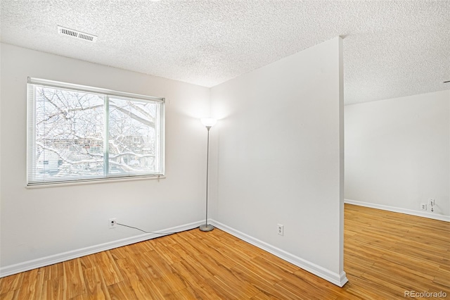 unfurnished room featuring a textured ceiling, baseboards, visible vents, and wood finished floors