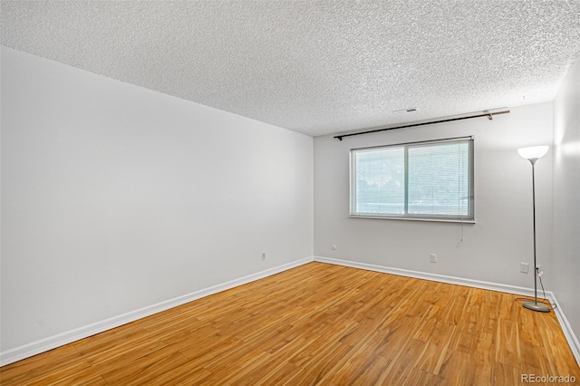spare room with a textured ceiling, baseboards, visible vents, and wood finished floors