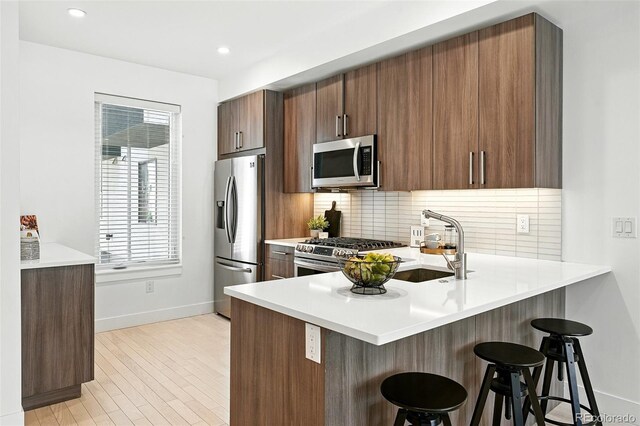 4394 Zenobia St, Denver, CO 80212 - kitchen with stainless steel appliances, a breakfast bar, decorative backsplash, a peninsula, and light countertops