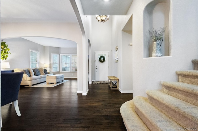 foyer entrance with dark wood-style floors, arched walkways, a notable chandelier, stairway, and baseboards