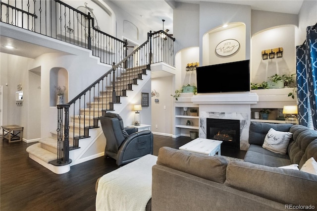 living area featuring a high ceiling, a premium fireplace, baseboards, stairs, and dark wood finished floors