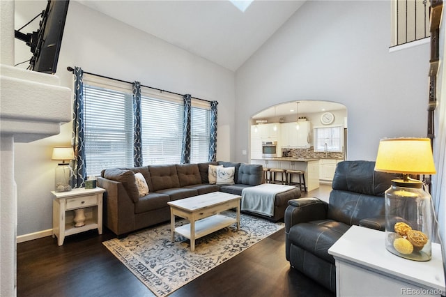 living area with arched walkways, high vaulted ceiling, dark wood-style flooring, and baseboards