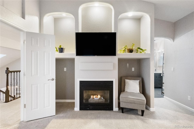 living room featuring vaulted ceiling, baseboards, a glass covered fireplace, and light colored carpet