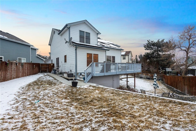 snow covered rear of property with a fenced backyard and a deck