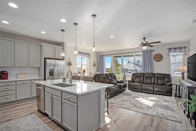 kitchen featuring light wood-type flooring, stainless steel appliances, sink, a center island with sink, and gray cabinets