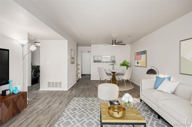 living room featuring wood finished floors, visible vents, baseboards, a ceiling fan, and washer / dryer