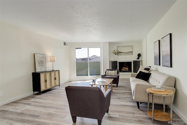 living area featuring light wood-style floors, baseboards, visible vents, and a fireplace with raised hearth