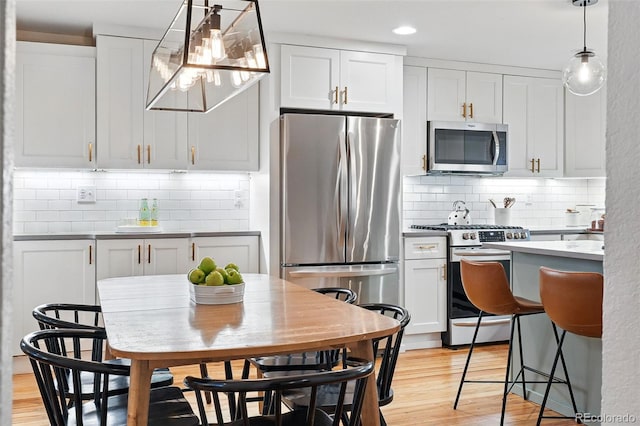 6830 Lamar St, Arvada, CO 80003 - kitchen featuring stainless steel appliances, backsplash, light wood-type flooring, pendant lighting, and white cabinets