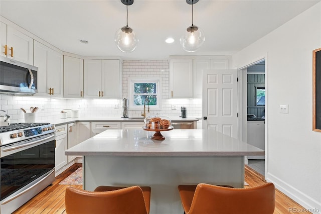6830 Lamar St, Arvada, CO 80003 - kitchen featuring appliances with stainless steel finishes, a kitchen bar, light wood-style flooring, decorative backsplash, and white cabinetry