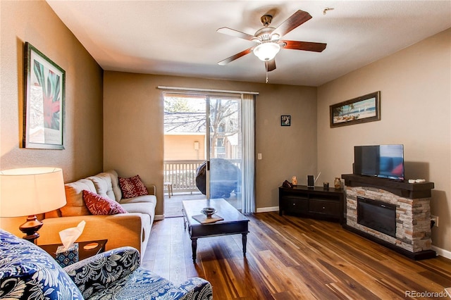 living room featuring ceiling fan, a fireplace, baseboards, and wood finished floors