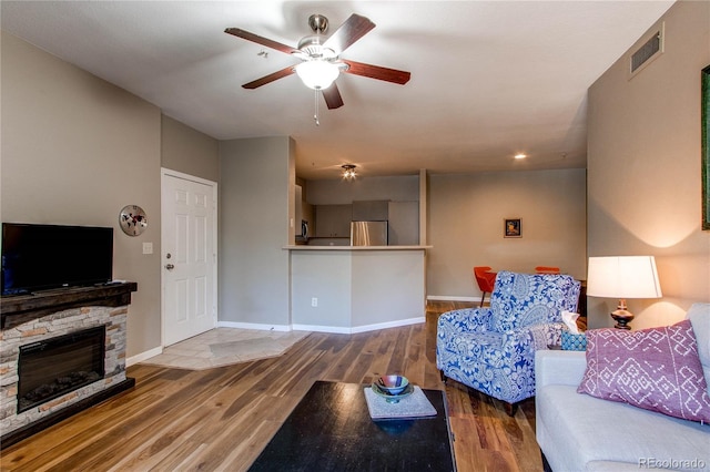 living area featuring a fireplace, visible vents, a ceiling fan, wood finished floors, and baseboards