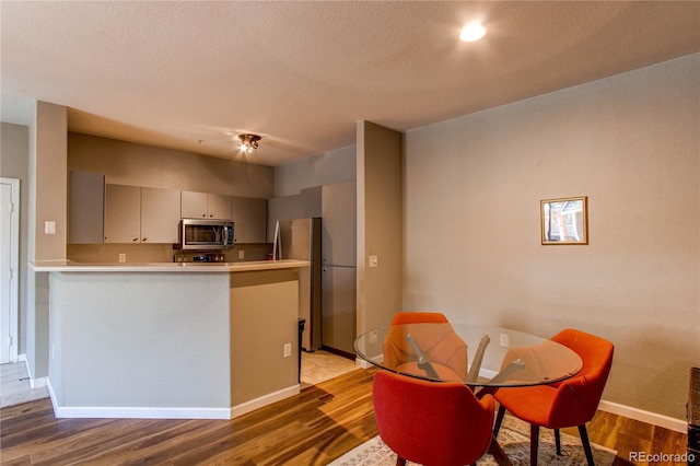 kitchen with stainless steel appliances, light countertops, dark wood finished floors, and a peninsula