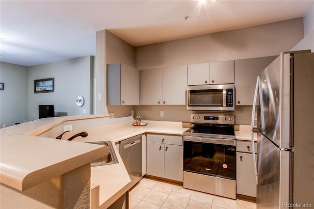 kitchen featuring light tile patterned floors, light countertops, appliances with stainless steel finishes, a sink, and a peninsula