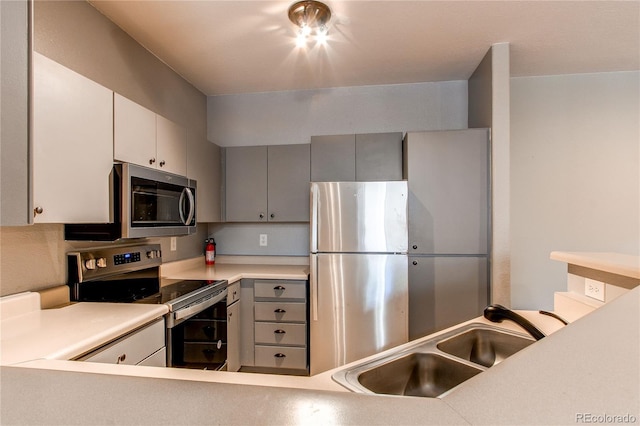 kitchen featuring stainless steel appliances, light countertops, a sink, and gray cabinetry