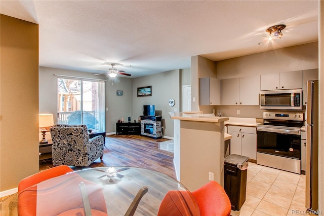 kitchen with a peninsula, baseboards, open floor plan, light countertops, and appliances with stainless steel finishes