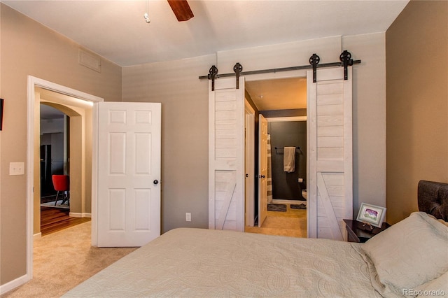 carpeted bedroom with a barn door, visible vents, arched walkways, and baseboards