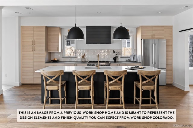 kitchen with sink, tasteful backsplash, stainless steel refrigerator, an island with sink, and pendant lighting