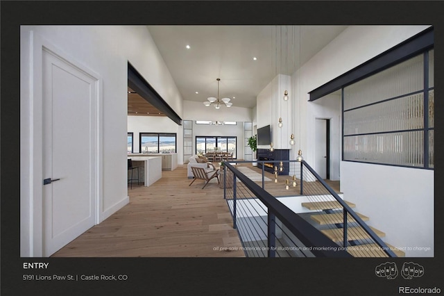 corridor featuring a notable chandelier, light hardwood / wood-style floors, and a high ceiling