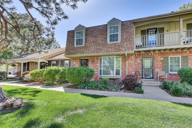 view of front of house featuring a shingled roof, brick siding, a balcony, a front lawn, and board and batten siding