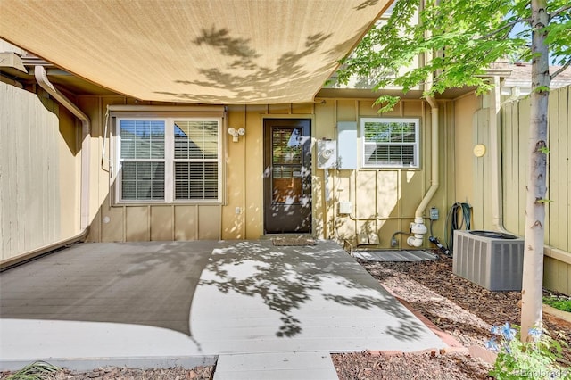 property entrance with central AC unit, a patio, and board and batten siding