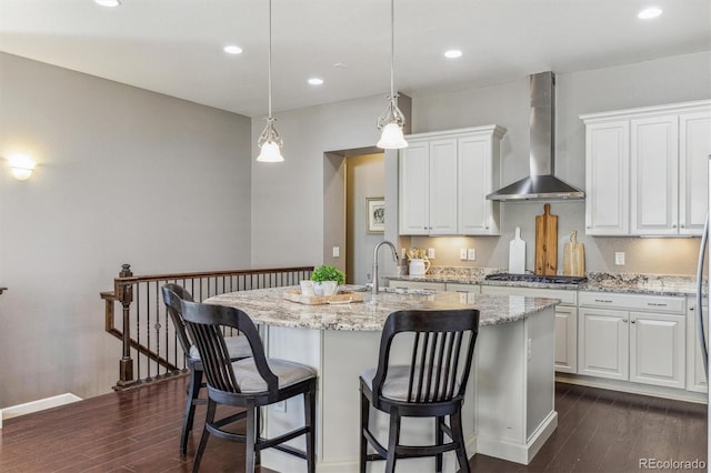 kitchen featuring white cabinets, wall chimney exhaust hood, and an island with sink