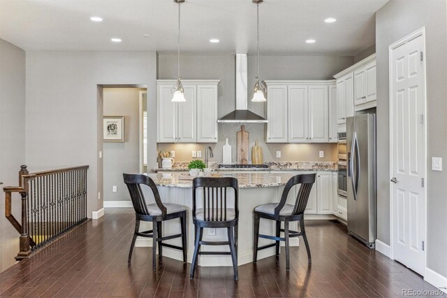 kitchen with white cabinetry, wall chimney exhaust hood, hanging light fixtures, stainless steel appliances, and a kitchen island with sink