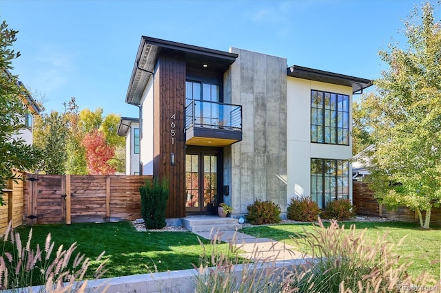 back of house featuring french doors, fence, a balcony, and a lawn