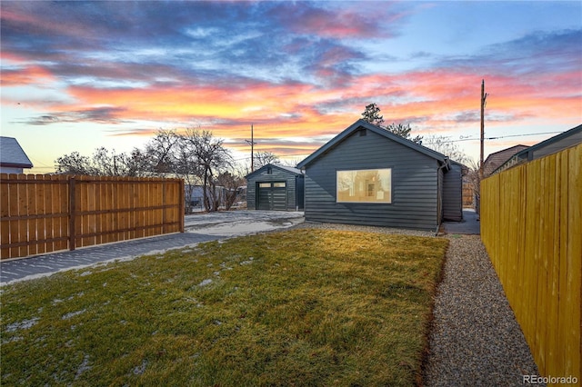 back house at dusk featuring a garage, an outdoor structure, and a yard