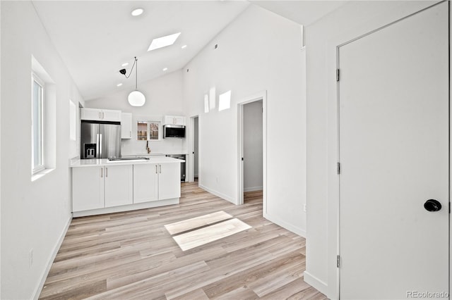 kitchen featuring a skylight, appliances with stainless steel finishes, pendant lighting, light hardwood / wood-style floors, and white cabinets