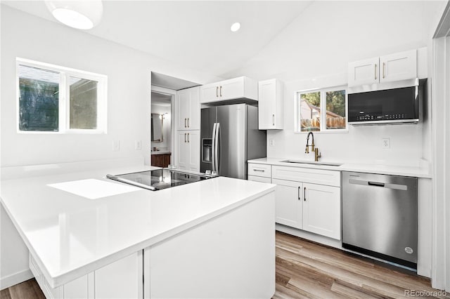 kitchen featuring a sink, wood finished floors, white cabinetry, appliances with stainless steel finishes, and vaulted ceiling